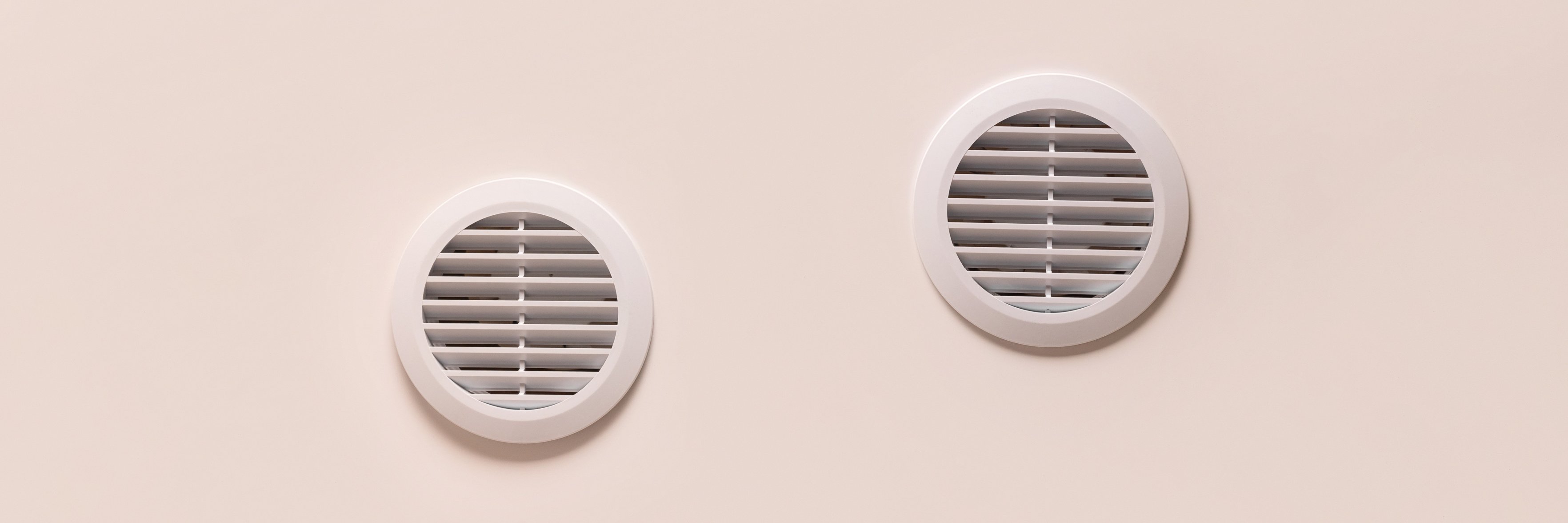 Round air vents with white plastic grate on beige ceiling